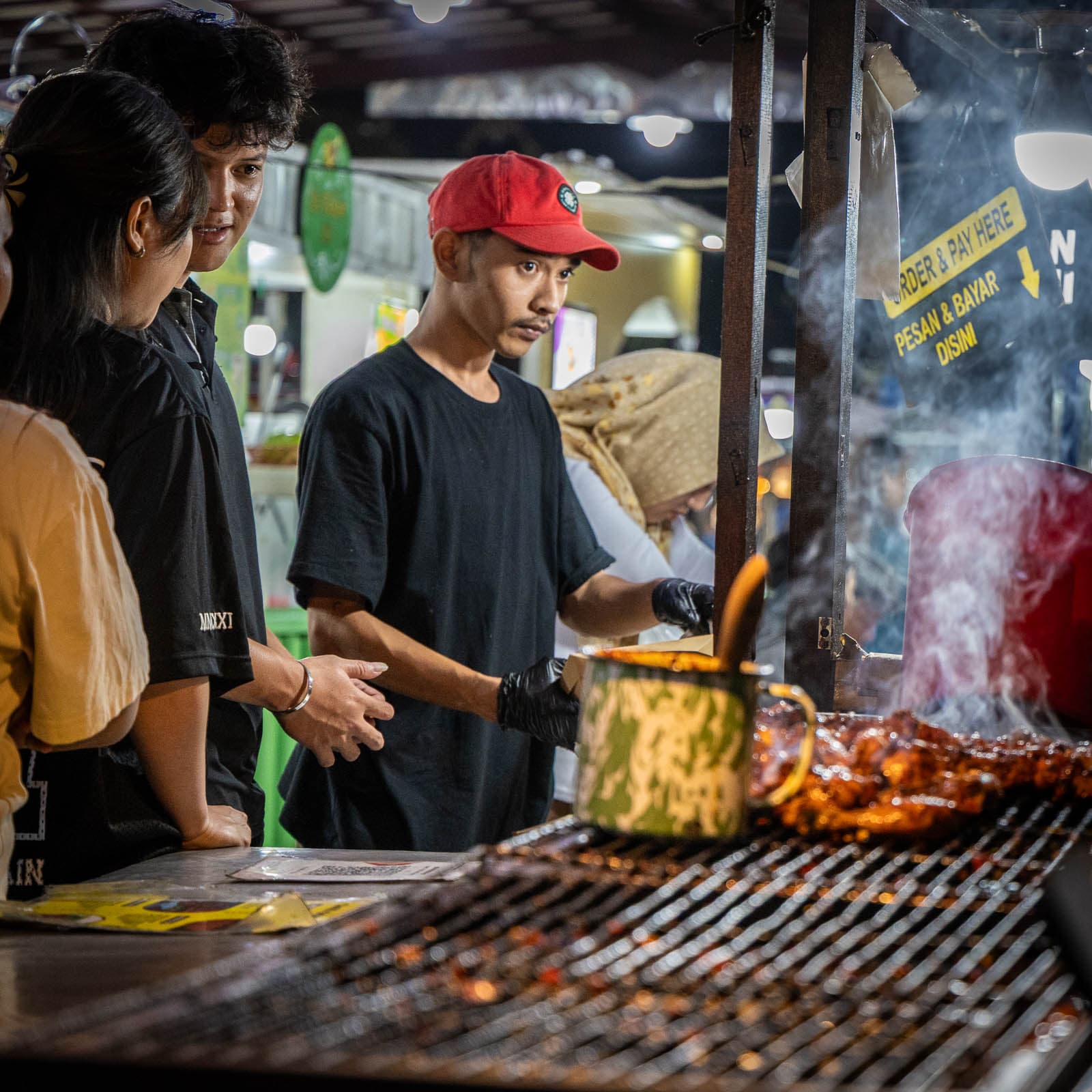 Evening street-food stalls on the illuminated riverside promenade beside Pasar Badung