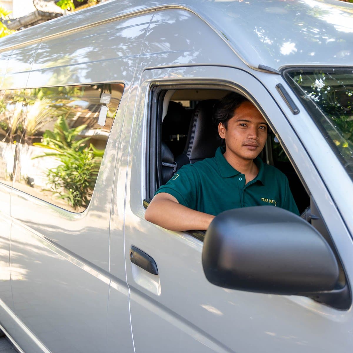 Take Me There driver in a branded polo at the wheel of a private transfer van in Bali